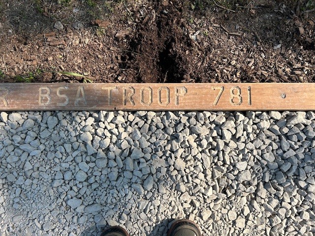 A wooden plaque with the inscription "BSA Troop 871." It is installed on the ground near the footpath to the Organizational camp.